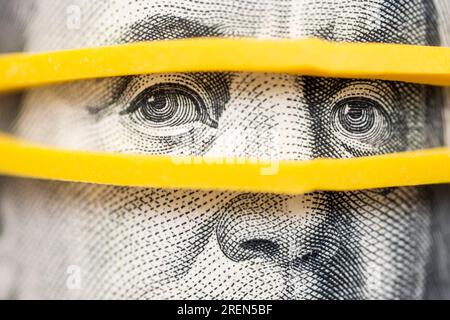 Portrait of Benjamin Franklin on a hundred dollar bill with eyes in rubber band Stock Photo