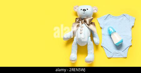 Bear toy and bodysuit with bottle of milk for baby on yellow