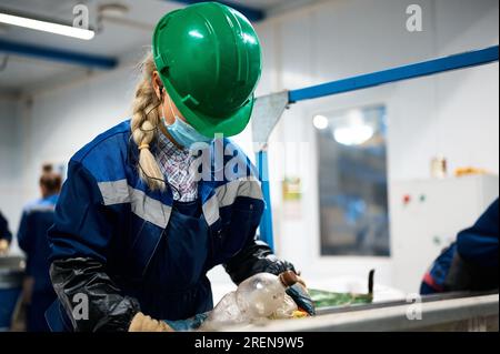 Woman in helmet sorts garbage at conveyor belt in workshop Stock Photo