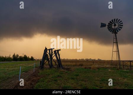 A dark storm cloud approaching over a windmill and old wooden tank stand on farmland at Moolort in Central Victoria, Australia Stock Photo