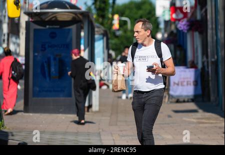 Man with rucksack or backpack, walking in the morning, maybe walking to work, busy city, carrying mobile phone, coffee and breakfast, in Summer, UK. Stock Photo