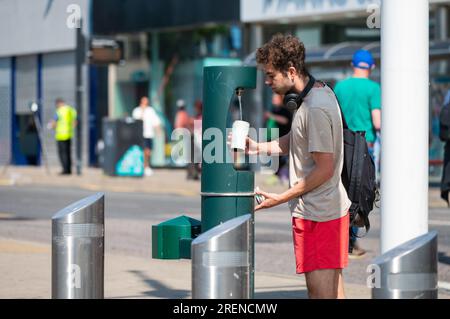 Young man filling a cup with water from a public water dispenser or drinking water fountain Summer in Brighton, Brighton & Hove, England, UK. Stock Photo