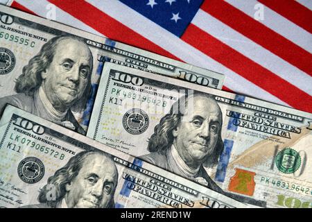 China. 29th July, 2023. In this photo illustration, three $100 bills are displayed on a table with the American flag in the background. Credit: SOPA Images Limited/Alamy Live News Stock Photo