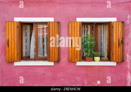 Detail with a colorful house windows with lots of flower pots and wooden shutters in Burano, Italy. Stock Photo