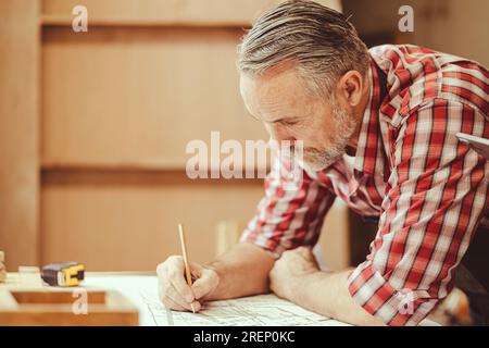 Senior professional engineer architect male working design drawing floor plan home furniture and renovate in workshop. Stock Photo