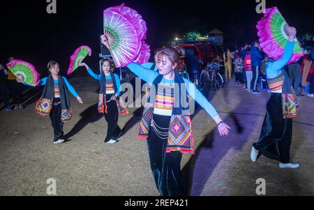 Young White Thai ethnic minority girls dance at night wearing traditional costumes and holding colourful fans at an open-air party held in Mai Chau in Stock Photo