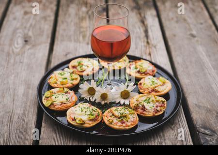 a small snack, pizzas piccolo on black plate with a glass of wine, on a wood table Stock Photo