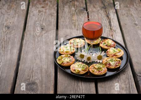 a small snack, pizzas piccolo on black plate with a glass of wine, on a wood table Stock Photo