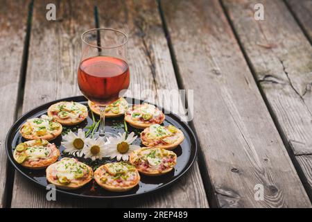a small snack, pizzas piccolo on black plate with a glass of wine, on a wood table Stock Photo