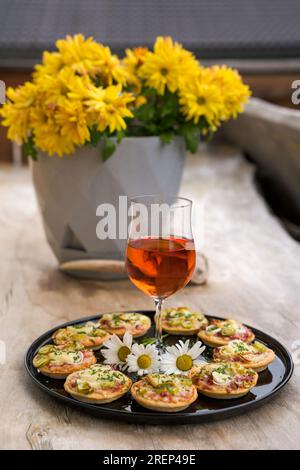 a small snack, pizzas piccolo on black plate with a glass of wine, on a wood table Stock Photo