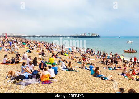 People sitting on the beach on a hot summer day with Brighton Palace Pier in background, Brighton, UK Stock Photo