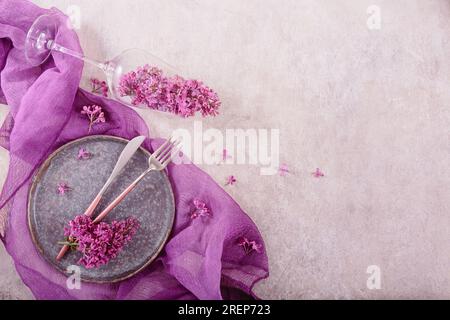 Table setting with drinking glass full of lilac flowers Stock Photo