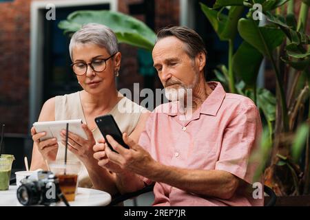 Mature couple using their smartphones while sitting together in an outdoor cafe Stock Photo