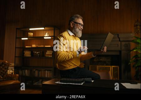 Smiling senior man using laptop while rest during work time at home office Stock Photo