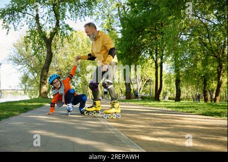 Senior man roller skating with little boy in urban park Stock Photo