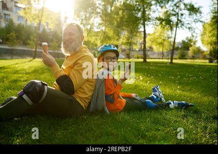 Tired and happy grandfather and grandson having ice-cream after roller skating Stock Photo