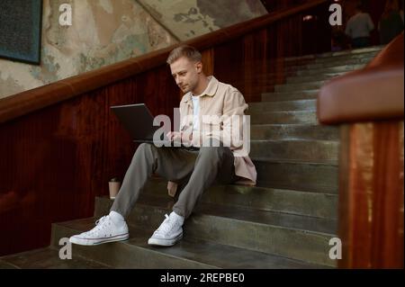 Man working on wireless laptop computer sitting on stairs in office Stock Photo