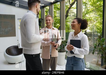 Smiling cheerful colleagues group standing at workplace and chatting Stock Photo