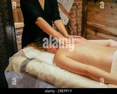 Young caucasian woman enjoy back massage. Professional massage therapist treat female patient wellness spa cabin. Relaxation, beauty, body and face tr Stock Photo