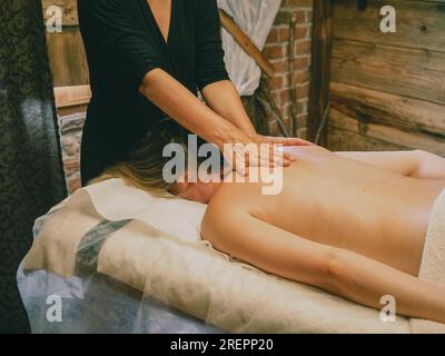 Young caucasian woman enjoy back massage. Professional massage therapist treat female patient wellness spa cabin. Relaxation, beauty, body and face tr Stock Photo