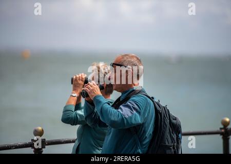 Man and woman looking through binoculars at Cowes seafront on the isle of wight coastline UK Stock Photo