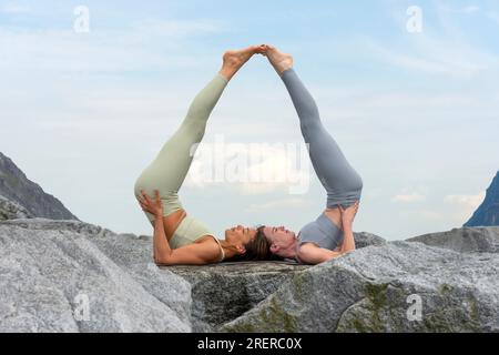 two women doing acro yoga outside, rocky mountain background. Stock Photo