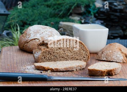 Wholemeal spelt bread on a wooden chopping board, knife garden in the background Stock Photo