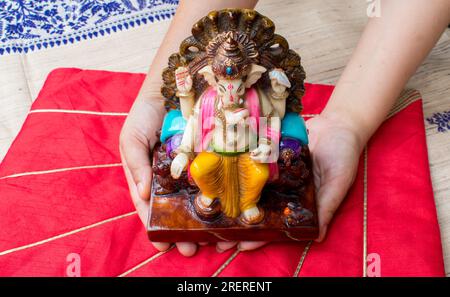 Holding beautiful idol or statue of God Ganesh in hand with red background . Happy Ganesh Chaturthi Greeting Card with copy space. Stock Photo