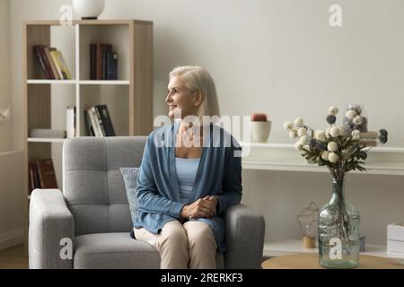 Cheerful dreamy blonde retired lady sitting in soft armchair Stock Photo