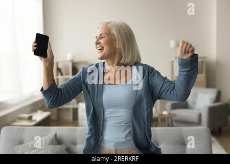 Excited happy pretty blonde senior woman dancing at home Stock Photo