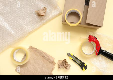Composition with packing tape dispenser, utility knife and paper on yellow background Stock Photo