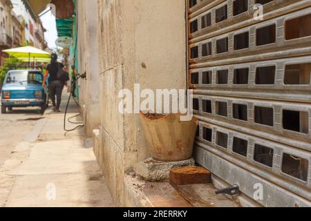 Havana, Cuba, A Cuban woman walks in the sidewalk where a Polski Fiat is parked. In the foreground a broken clay container or plant pot Stock Photo