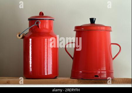 Red vintage metal milk jug with wooden handle and coffee pot with lid on a wooden shelf Stock Photo
