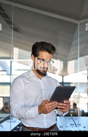 Serious busy young Latin business man using tablet standing in office. Stock Photo