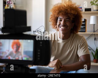 Young African American man recording video for social networks with a camera in an apartment. Digital content creator, streaming Stock Photo