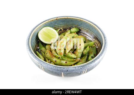 Bowl of delicious stir fried sugar snap peas with seasoning and slice of lime isolated on white background Stock Photo