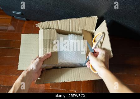 Opening cardboard parcel box with scissors Stock Photo