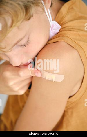 Crop child with sterile mask applying medical patch on shoulder during COVID 19 pandemic Stock Photo