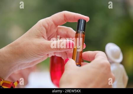 Crop unrecognizable female with manicure showing small bottle of beauty oil on blurred background outdoors Stock Photo