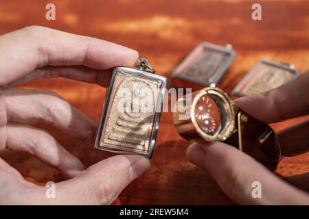 Using a loupe to see the detail on an old Thai Buddha amulet Stock Photo