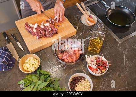 From above of crop anonymous person cutting raw octopus on wooden board while cooking in kitchen Stock Photo
