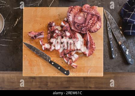 Top view of fresh raw bits of octopus placed on wooden cutting board with knives in granite table Stock Photo