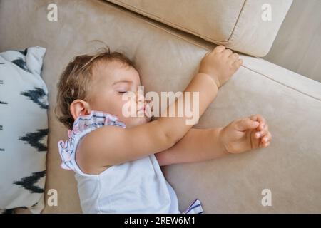 Top view of little baby girl lying on cozy couch and napping in living room at home Stock Photo