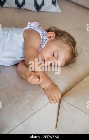 From above of adorable baby girl lying on cozy sofa and sleeping in living room at home Stock Photo