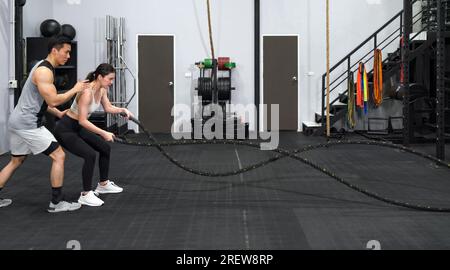 Fitness-focused couple immersed in an intense rope workout at a well-equipped modern gym. Stock Photo