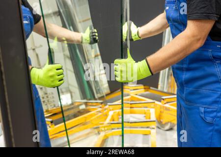 A glazier picks up sheets of thick glass from a rack in a glass factory, many mirrors cause mirror reflections Stock Photo