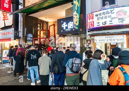 Long line of mainly Japanese people queuing outside the popular Chibo okonomiyaki restaurant in the evening in Dotonbori, Osaka. Stock Photo