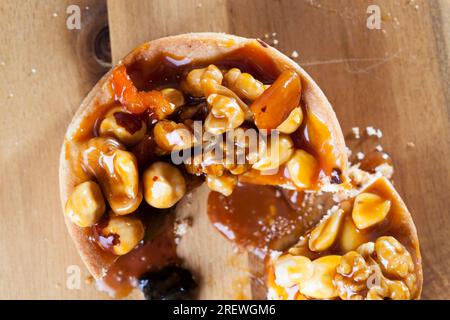 the ingredients used in the tartlet are hazelnuts, peanuts, dried apricots, dried plums, walnuts, round shaped tartlet with nuts and dried fruits pour Stock Photo