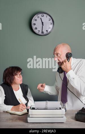 A secretary and editor from the past at work. Article on time. Table with telephone and typewriter. Vintage Stock Photo