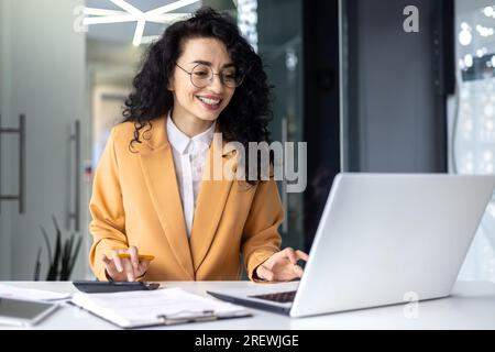 Mature successful financier accountant on paper work with papers, documents contracts and charts graphs, businesswoman boss with calculator smiling happy with achievement results, inside office. Stock Photo
